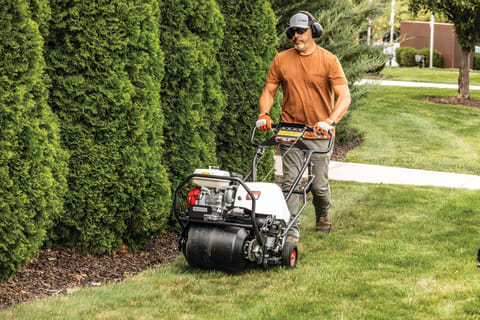 A Man Controls a Bobcat AE19 Lawn Aerator Along a Row of Hedges