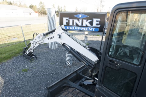 A Bobcat compact excavator sits beside a Finke Equipment sign alongside Finke’s driveway 