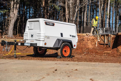 The Bobcat PA185v portable air compressor powers a jackhammer on a construction site.