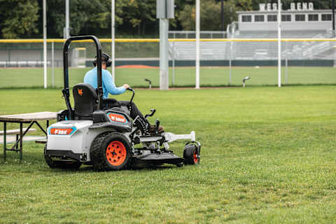 The Bobcat ZT6000e electric zero-turn mower cuts grass near a sports field.