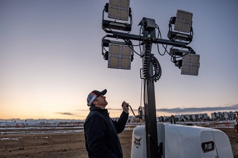 Hard Worker Turning on Bobcat Light Tower at Dusk to Brighten His Field
