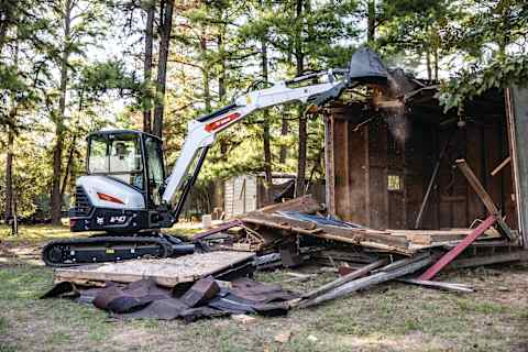 A Bobcat E40 compact excavator demolishes a small building structure.  