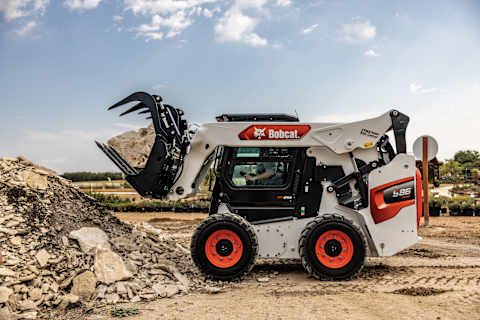 An S86 Skid-Steer Loader Moves Rocks Using an Industrial Grapple Attachment