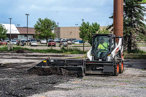 Bobcat S64 Skid-Steer Loader spreads asphalt on parking lot.