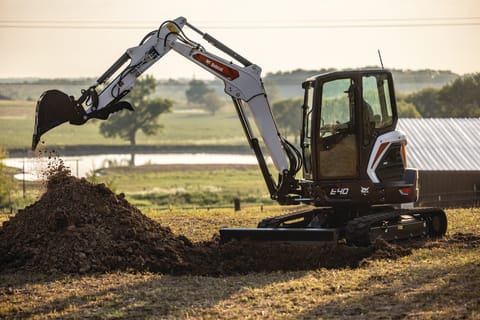 A Bobcat E40 Compact Excavator Reaches and Digs a Deep Hole With a Bucket