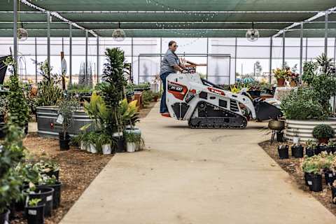 A Bobcat MT100 Mini Track Loader Transports Soil at Shades of Green Nursery With Lush Plants and Landscaping Supplies in the Background