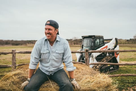 Chip Gaines sitting on a hay bale with a T86 Bobcat compact track loader in the background.
