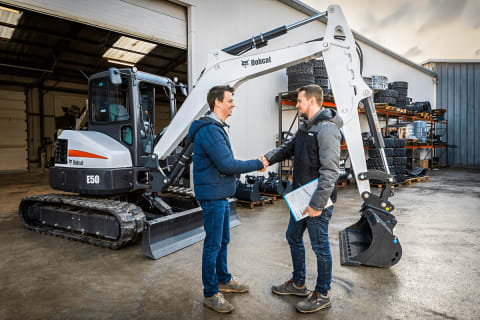 Two men shake hands in front of a Bobcat E50 Mini Excavator after they made a deal.