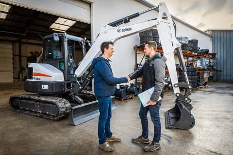 Dos hombres se dan la mano delante de una miniexcavadora Bobcat E50 tras llegar a un acuerdo.