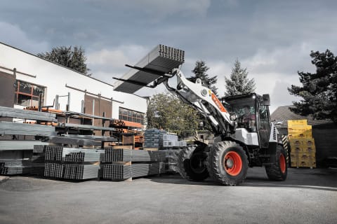 An action shot of Bobcat's L85 compact wheel loader and a male operator transporting metal poles.