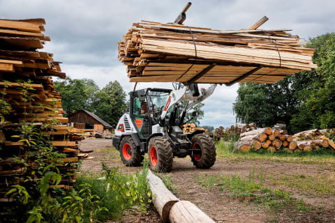 Una fotografía exterior de la cargadora de ruedas compacta L95 de Bobcat transportando troncos y madera.