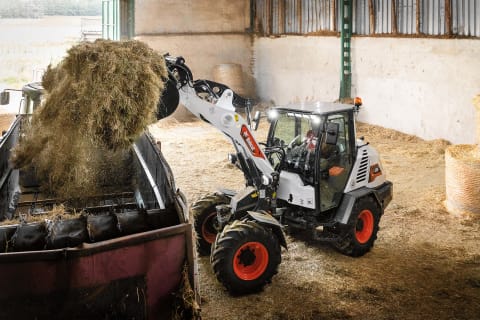 
Actiefoto van de Bobcat L95 compacte wiellader die hooi in een schuur vervoert.