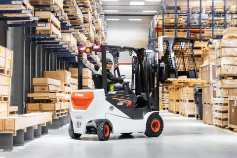 An indoor action shot of an operator lifting a load with the electric B25NS forklift. 