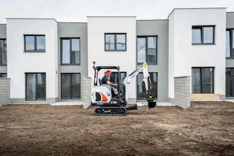 An outdoor action shot of an operator preparing the electric E19e to dig into the ground with the digging bucket attachment. 