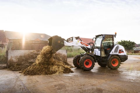 An outdoor action shot of a male operator scooping up a pile of hay using Bobcat's L95 compact wheel loader. 