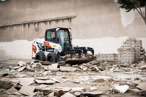 An outdoor, action shot of Bobcat's S550 with a male operator moving rubble using a bucket attachment. 