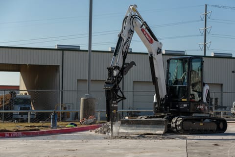 An Operator Uses a Bobcat Compact Excavator With a Breaker Attachment to Bust up a Concrete Road