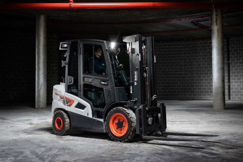 A dimly lit indoor shot of a male operator using a Bobcat diesel forklift in a concrete space.