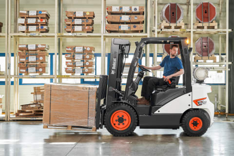 An indoor profile shot capturing a male operator skillfully reversing a Bobcat diesel forklift in a well-lit and organized warehouse.