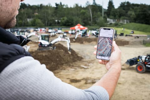 Een man die de Bobcat Machine IQ-app gebruikt om zijn E50z-minigraafmachine te controleren.