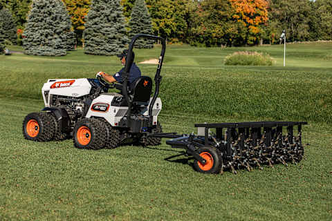 Operator uses a Bobcat AT450 articulating tractor to pull an AE72 aerator near a putting green on a golf course 