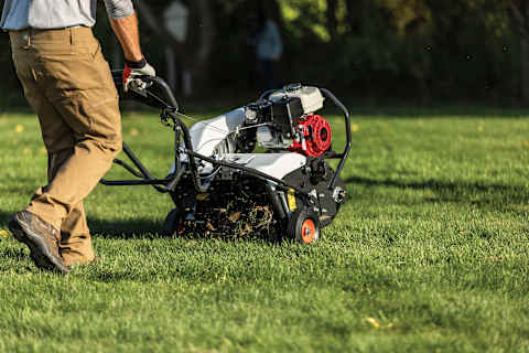 An Operator Steers an AE19 Aerator on a Green Lawn 