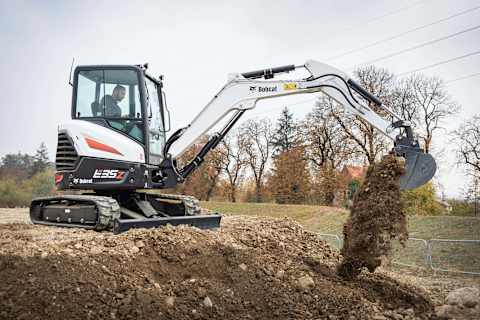 A side profile of a male operator using a Bobcat E35Z excavator with a bucket attachment to scoop dirt.