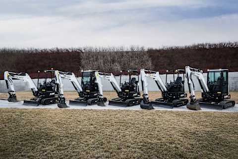 Five Bobcat excavators—E26, E27z, E27, E34, and E35z—lined up on the sidewalk with their lights on and their buckets and booms lowered.