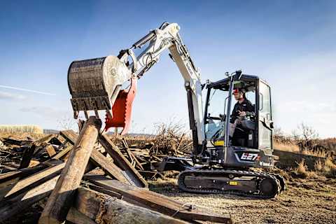 A male operator using a Bobcat E27Z excavator to move debris.