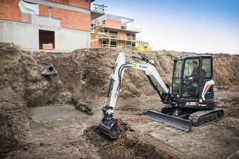 A male operator using an E35Z excavator to scoop dirt at a construction site for apartment buildings.