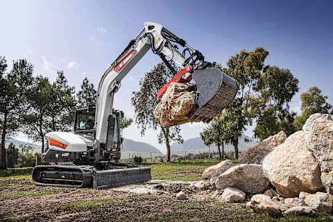 A male operator using a Bobcat E88 to move a massive boulder. 