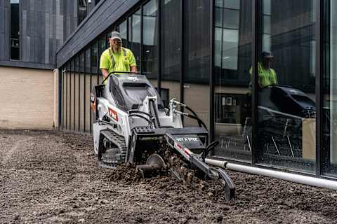 Operator on Bobcat MT120 with trencher attachment on commercial construction site