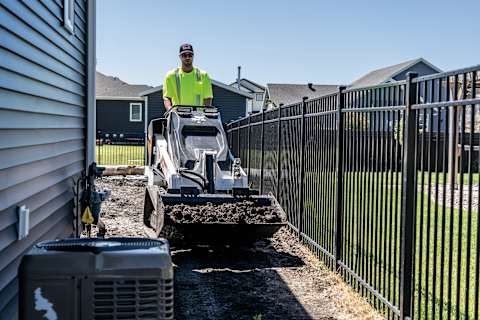 A Bobcat MT120 Carries Dirt Between a Fence and Air Conditioner on a Residential Jobsite