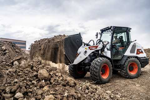 Left side view of a Bobcat L95 Compact Wheel Loader hauling dirt at a gravel pit