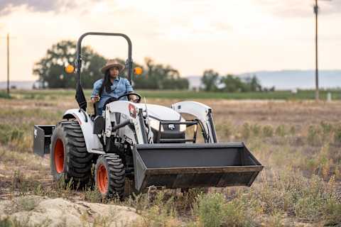 Vista frontal derecha de un operario realizando trabajos de jardinería en una propiedad residencial con un tractor compacto Bobcat CT2025.