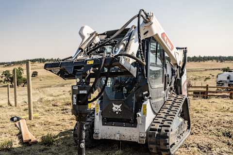 Bobcat T66 compact track loader digging post holes with auger attachment, powered by standard-flow hydraulics.