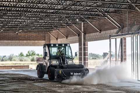 Bobcat UW56 Toolcat utility work machine with sweeper attachment clearing dirt and debris from a construction site floor