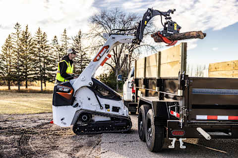 Bobcat MT120 mini track loader with log grapple attachment lowering log onto logging truck trailer.