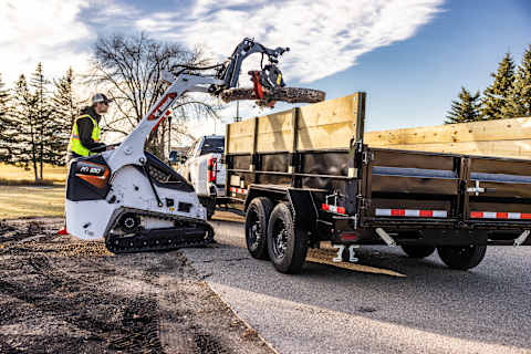 An Operator Lowers a Log Onto a Small Pickup Trailer With a Bobcat Mini Track Loader and Log Grapple Attachment