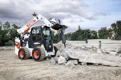 Operatore che utilizza una pala compatta gommata Bobcat S86 dotata di martello idraulico per rompere in modo efficace cemento in un cantiere edile all'aperto