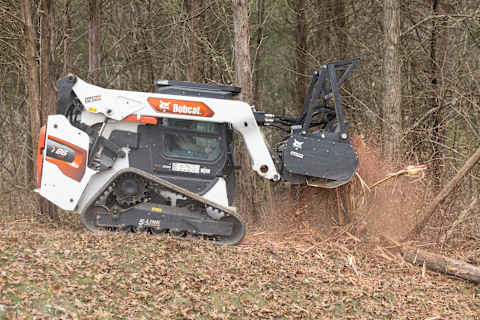 A T86 Compact Track Loader Uses a Drum Mulcher to Shred Trees in a Wooded Area