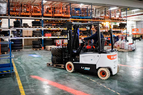 Photo en action d’un opérateur utilisant le chariot élévateur Bobcat B20X-7 alimenté par une batterie lithium-ion pour déplacer avec expertise une caisse en bois.