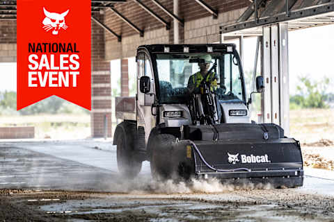 A Toolcat Utility Work Machine With a Sweeper Attachment Clears Dirt From a Sidewalk