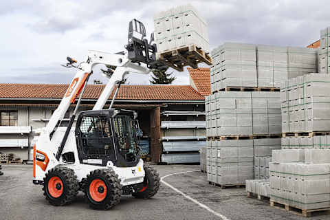 Opérateur aux commandes d’une chargeuse compacte sur pneus S630 de Bobcat pour soulever une palette de blocs de béton dans un dépôt de construction.