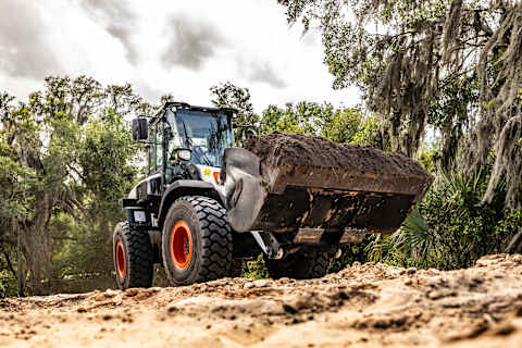 An Operator Travels Across a Jobsite in a Bobcat L235 Large Wheel Loader With a Full Bucket of Dirt