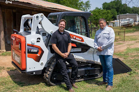 Entrepreneur and Magnolia co-founder Chip Gaines (left) and Hoof Haven Sanctuary and U.S. Veteran Jason Shields (right) stand by a Bobcat T595 compact track loader.