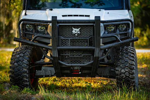 A Bobcat UV34XL Utility Vehicle Equipped With a Front Brush Guard Parked on Grass at a Rural Property