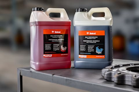 Bobcat Max Performance Hydraulic Fluid Containers for Warm and Cool Climates Displayed on a Workbench
