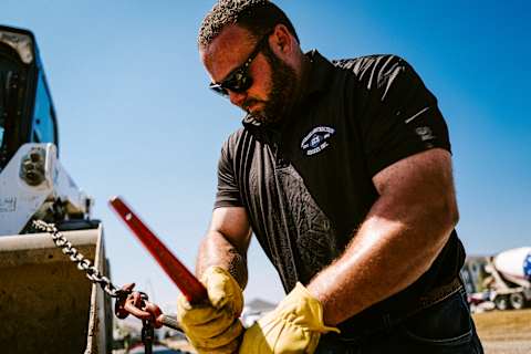 An Operator Secures Equipment Using a Chain and Tool Next to a Bobcat Machine at a Jobsite