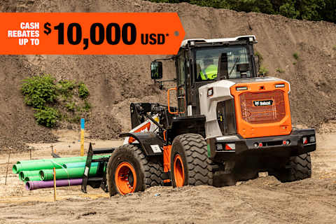 A Rear View of a Bobcat Large Wheel Loader Carrying Pipes Across a Jobsite; A Cash Rebate Banner Is in the Top-Left Corner